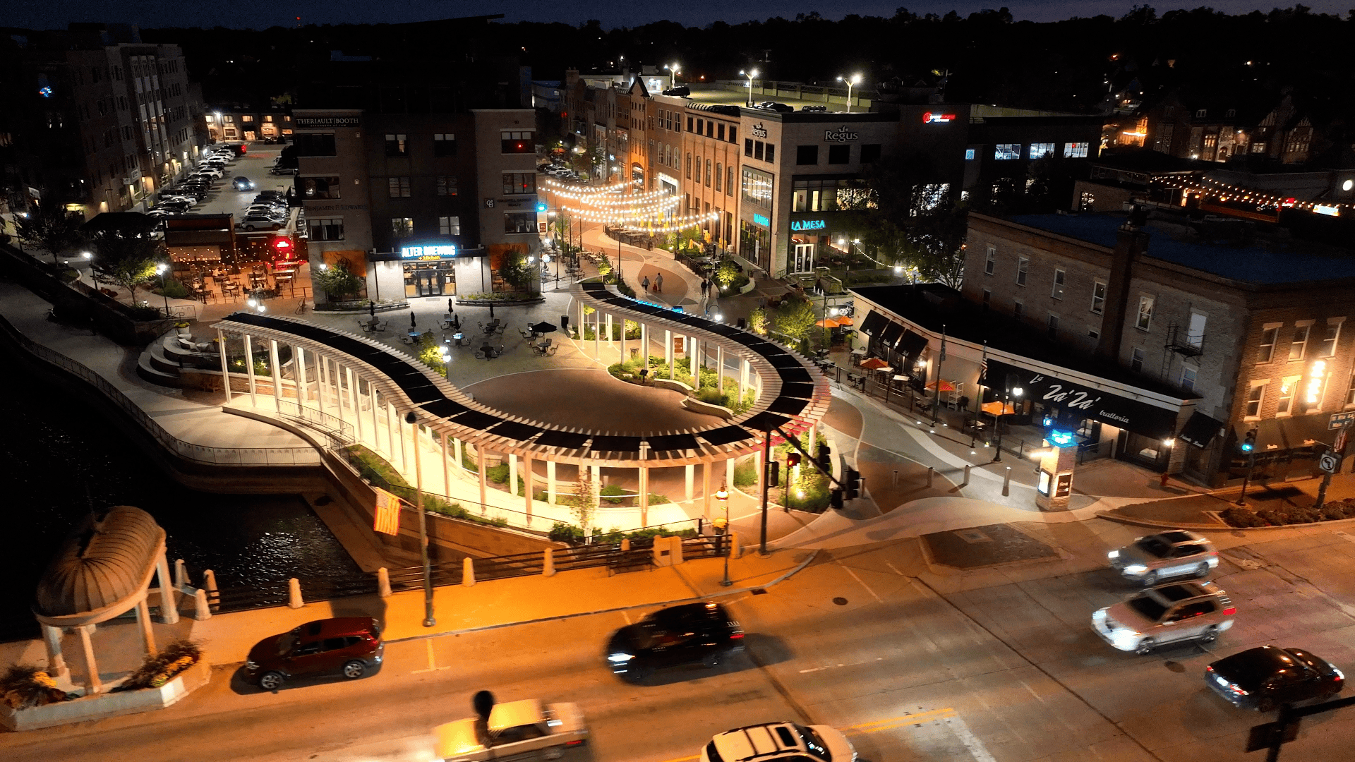 Night view of a lively city street with shops, cars, and bright lighting in an urban setting.