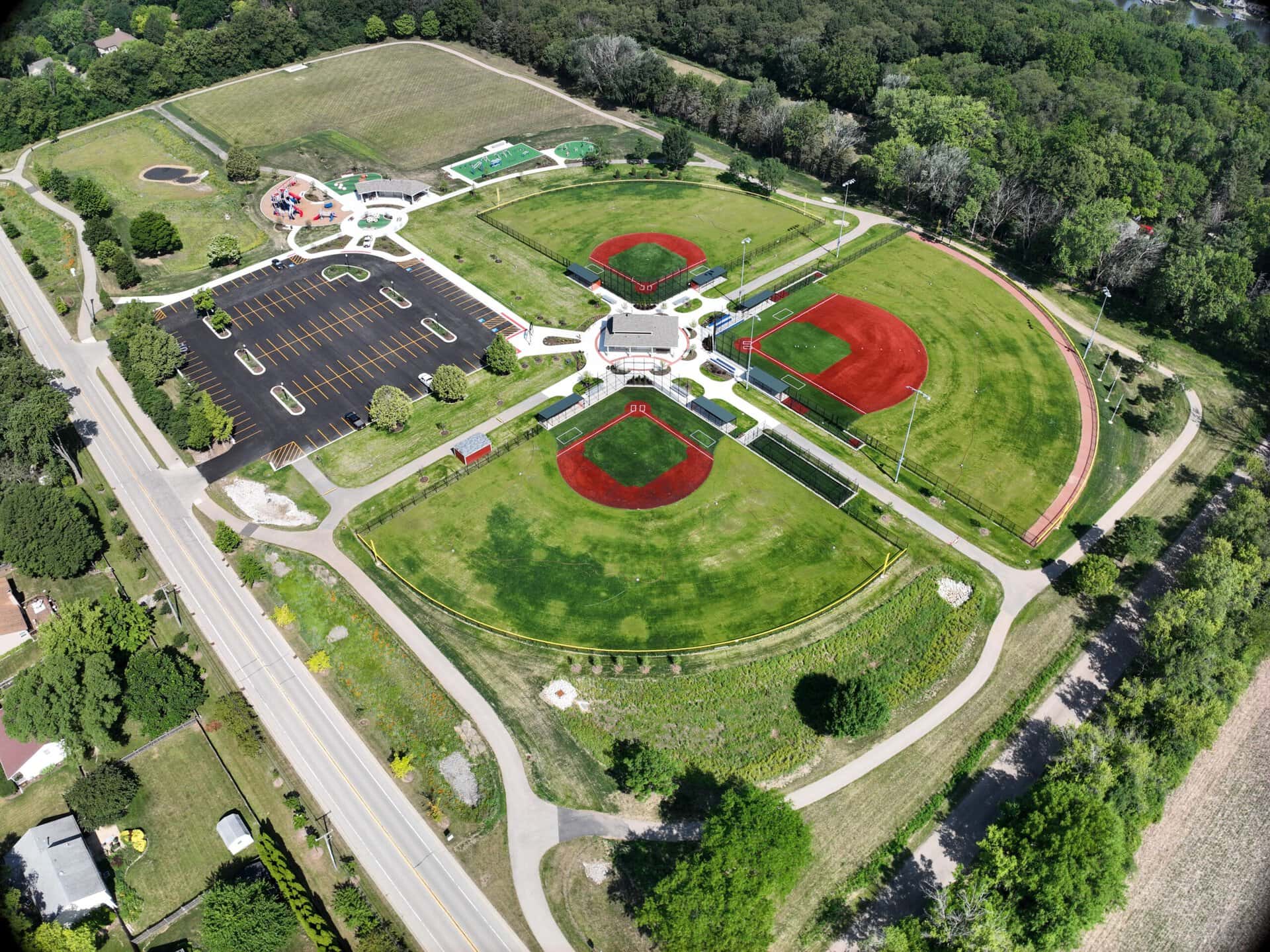 Aerial view of a park with sports fields and playground, surrounded by trees.