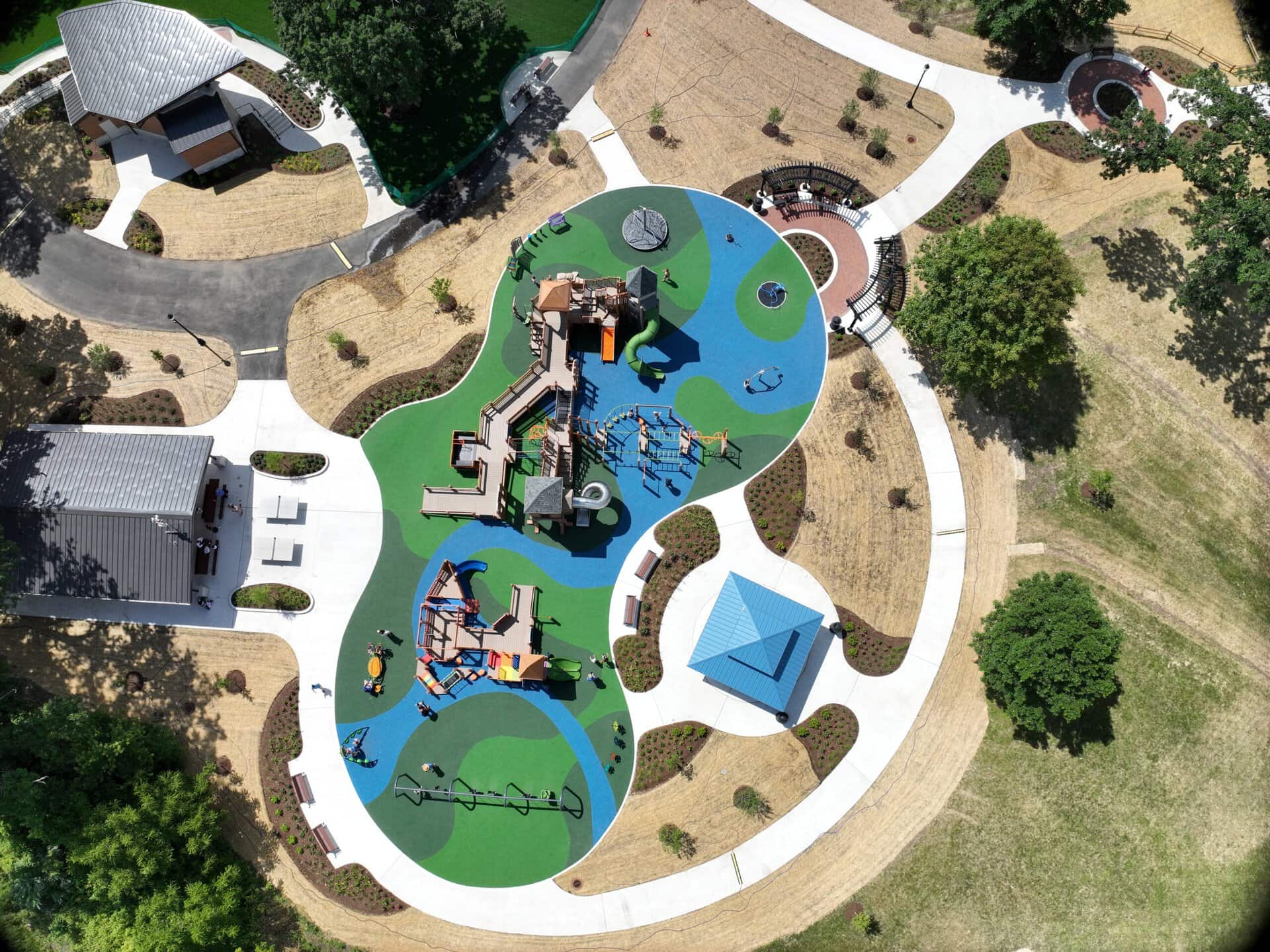 Aerial view of a colorful playground with slides, swings, and climbing structures in a park.